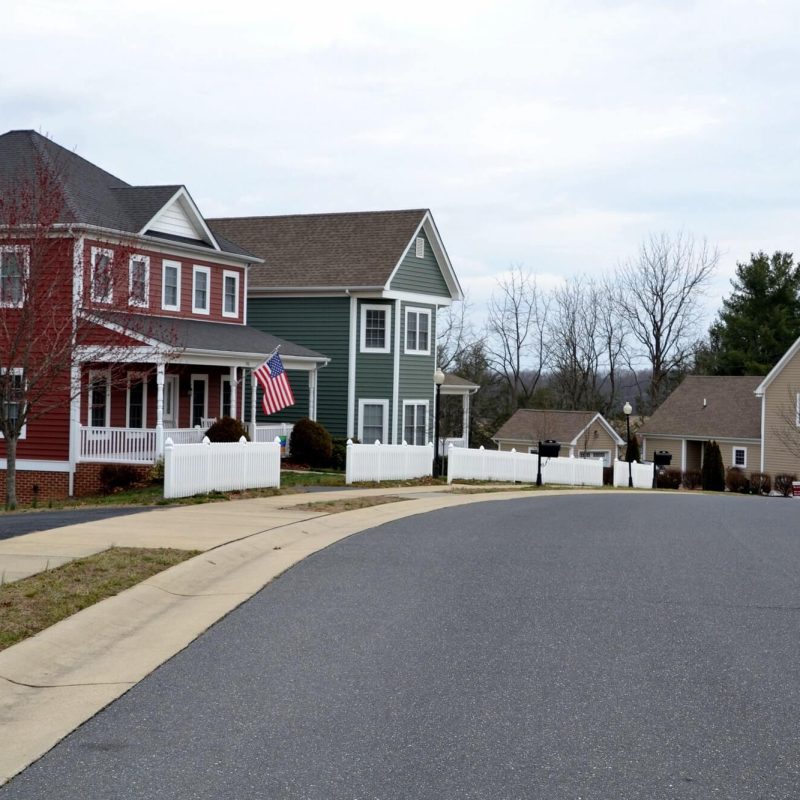 Row of modern houses in various colors lining a peaceful, tree-lined street in a well-designed neighborhood.