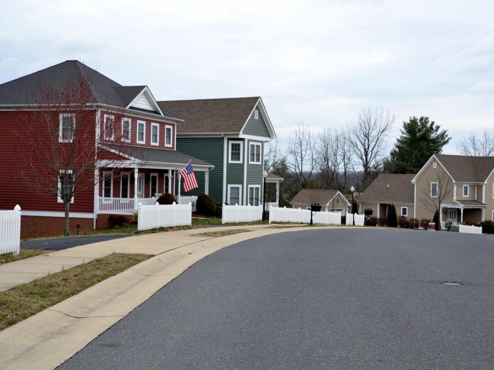 Row of modern houses in various colors lining a peaceful, tree-lined street in a well-designed neighborhood.